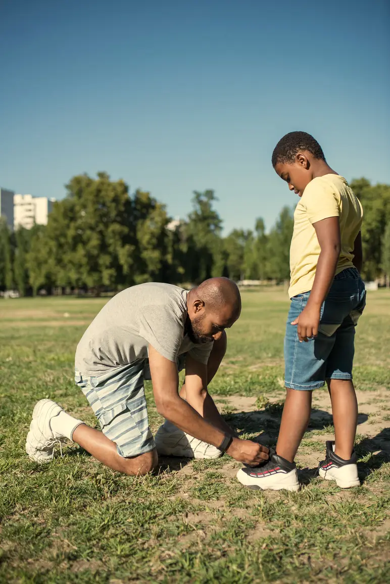 Pai ajoelhado amarrando o tênis do filho no campo
